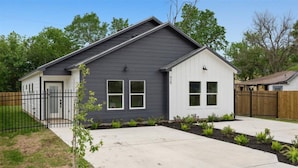 Une maison de plain-pied à l’extérieur gris et aux bordures blanches, avec une petite cour avant agrémentée d’un arbre et une clôture en métal noir.