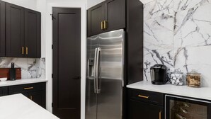 A modern kitchen with dark cabinetry, a stainless steel refrigerator, and marble backsplash. - Family Retreat Near NRG Med Center (Houston)