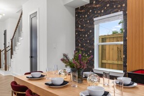 Comedor con mesa de madera dispuesta para cuatro personas, un florero con flores y un mural de un cielo estrellado.