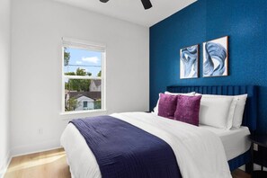 Un dormitorio con una cama grande, un ventanal con persianas y dos cuadros abstractos en la pared.
