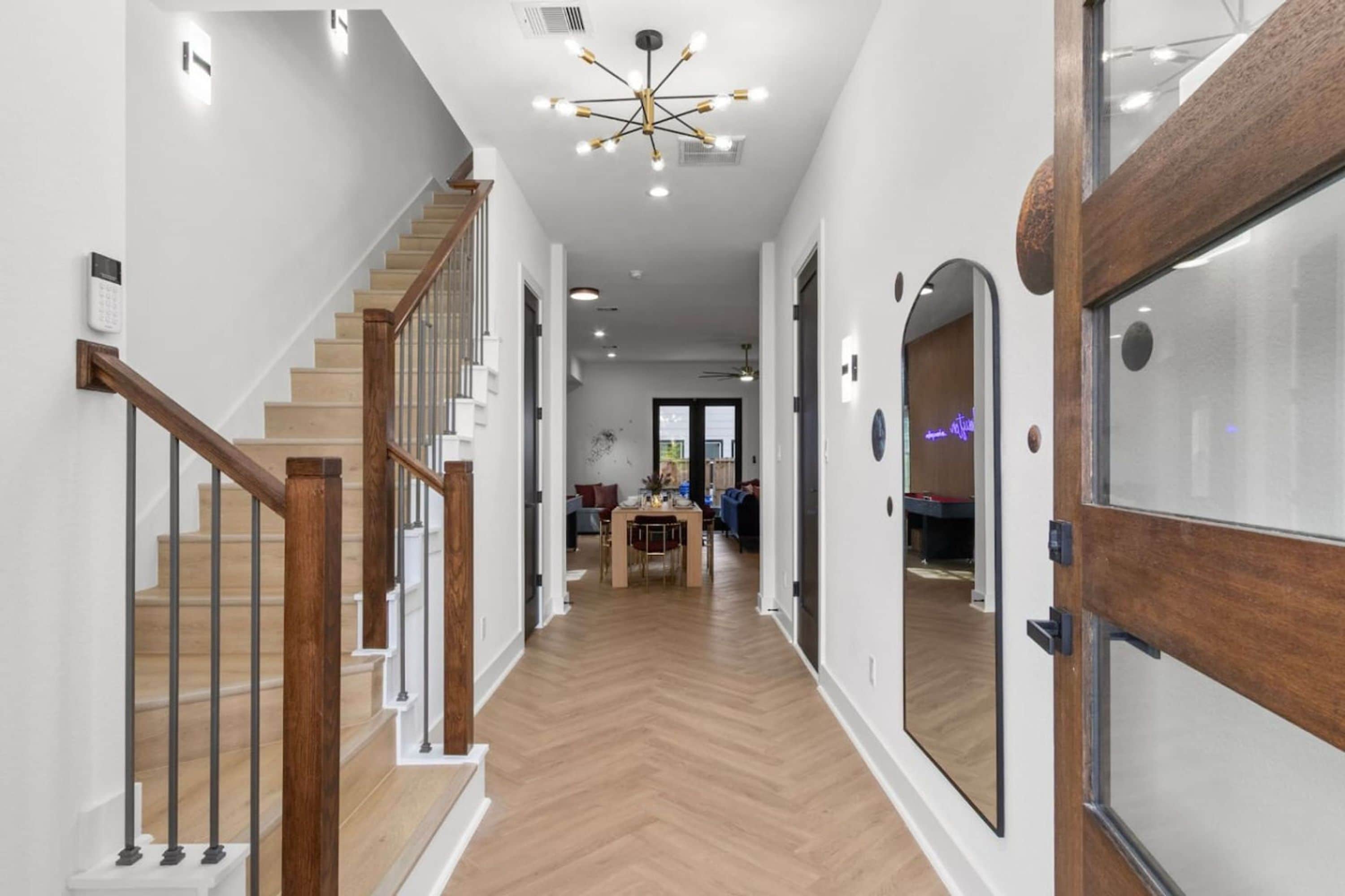 A modern interior with a wooden staircase, a dining area, and a large mirror.