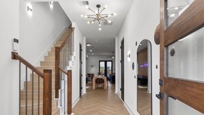 A modern interior with a wooden staircase, a dining area, and a large mirror. - Family Retreat Near NRG Med Center (Houston)