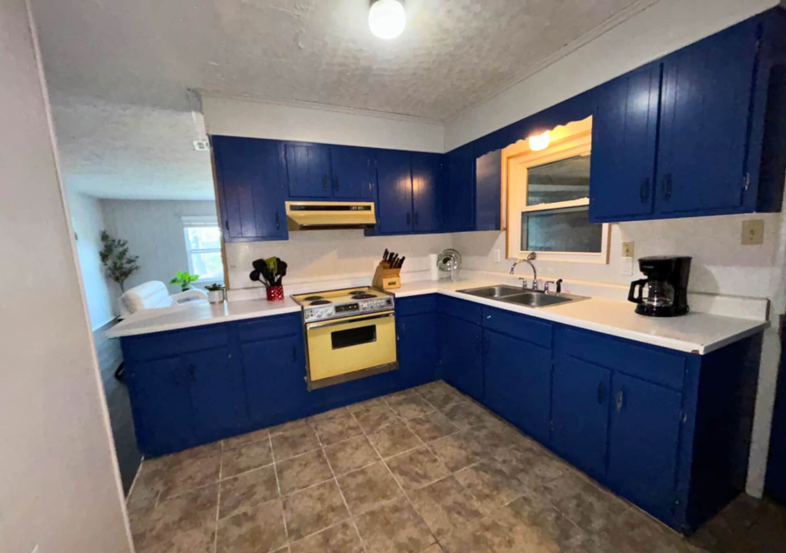A kitchen with blue cabinets, a white countertop, a yellow stove, and a sink.