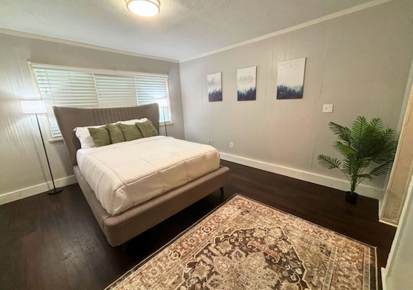 A bedroom with a bed, a floor lamp, a large rug, and three wall art pieces. - Retro 1BR Near Downtown Quiet Comfy Stay (Houston)
