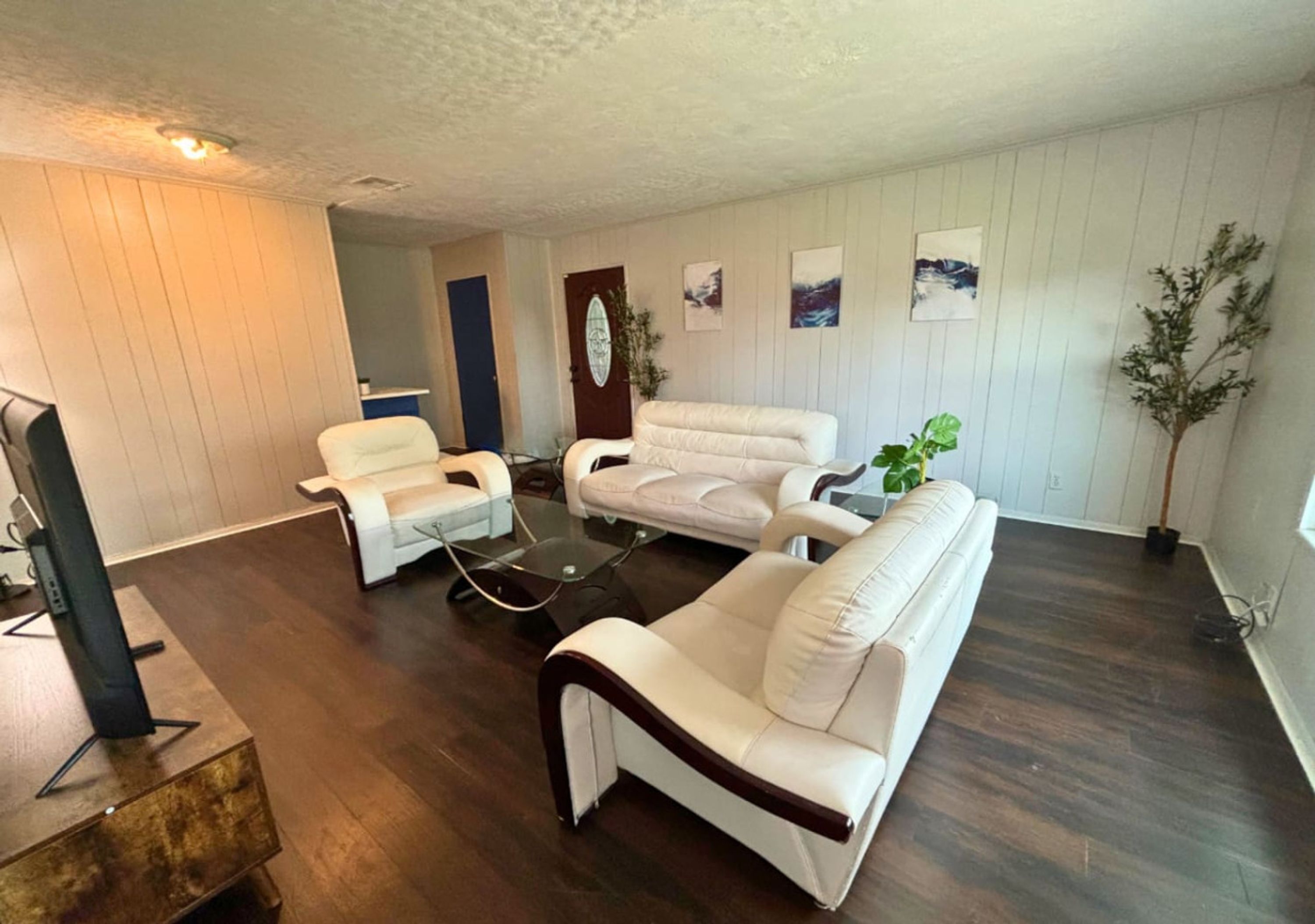 A living room with a sofa, armchair, and coffee table. There is a television on a stand, a plant, and artwork on the wall.
