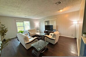 A living room with a sofa set, a glass coffee table, and a flat-screen TV. - Retro 1BR Near Downtown Quiet Comfy Stay (Houston)