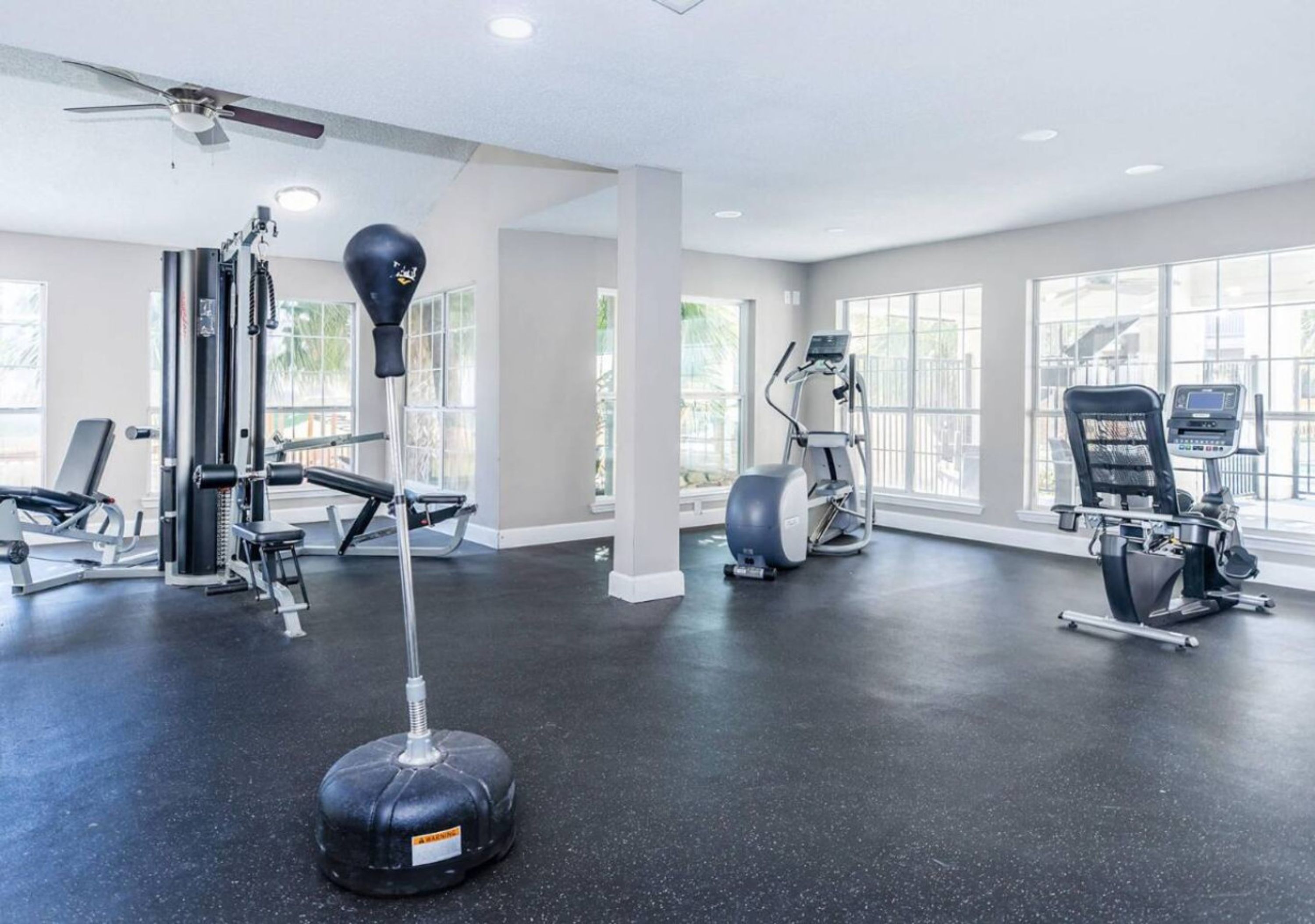 A gym with various exercise equipment, large windows, and a ceiling fan.