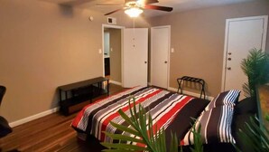 Ein Schlafzimmer mit Bett, Deckenventilator, Sitzbank, Stuhl und Tür.