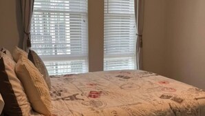 A bedroom with a bed, two windows with blinds, and curtains. - 2x2 in Medical Center - The Magnolia Resort (Fort Worth)