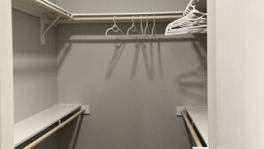 A walk-in closet with open shelves, a hanging rod, and a door. - 2x2 in Medical Center - The Magnolia Resort (Fort Worth)