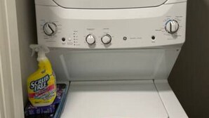 A white washing machine with control knobs and a detergent bottle on top. - 2x2 in Medical Center - The Magnolia Resort (Fort Worth)