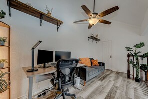 A home office with a desk, two monitors, a chair, a ceiling fan, and a sofa. - Upscale 1BR Condo in Med Center (Houston)