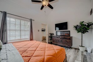 A bedroom with a bed, a ceiling fan, a TV, a dresser, and a potted plant. - Upscale 1BR Condo in Med Center (Houston)