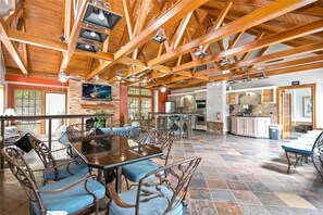 A spacious dining area with a high wooden ceiling, a large table, and blue upholstered chairs. - Upscale 1BR Condo in Med Center (Houston)