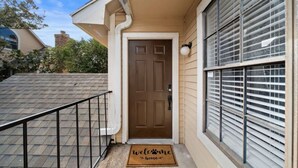 A house with a brown door, a welcome mat, and a window with blinds. - Upscale 1BR Condo in Med Center (Houston)
