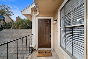 A house with a brown door, a welcome mat, and a window with blinds.