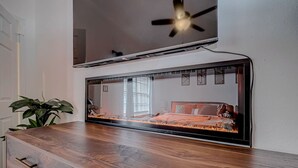 Egy hálószoba, amelyben van egy ágy, egy mennyezeti ventilátor és egy a falra szerelt televízió.