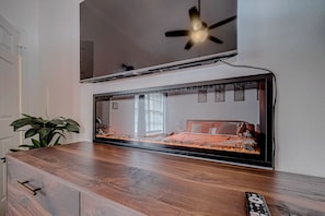 Un dormitorio con cama, ventilador de techo y televisor montado en la pared.