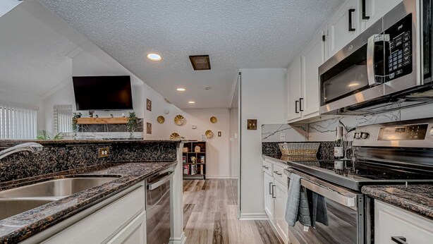 A modern kitchen with granite countertops, stainless steel appliances, and a flat-screen TV mounted on the wall. - Upscale 1BR Condo in Med Center (Houston)