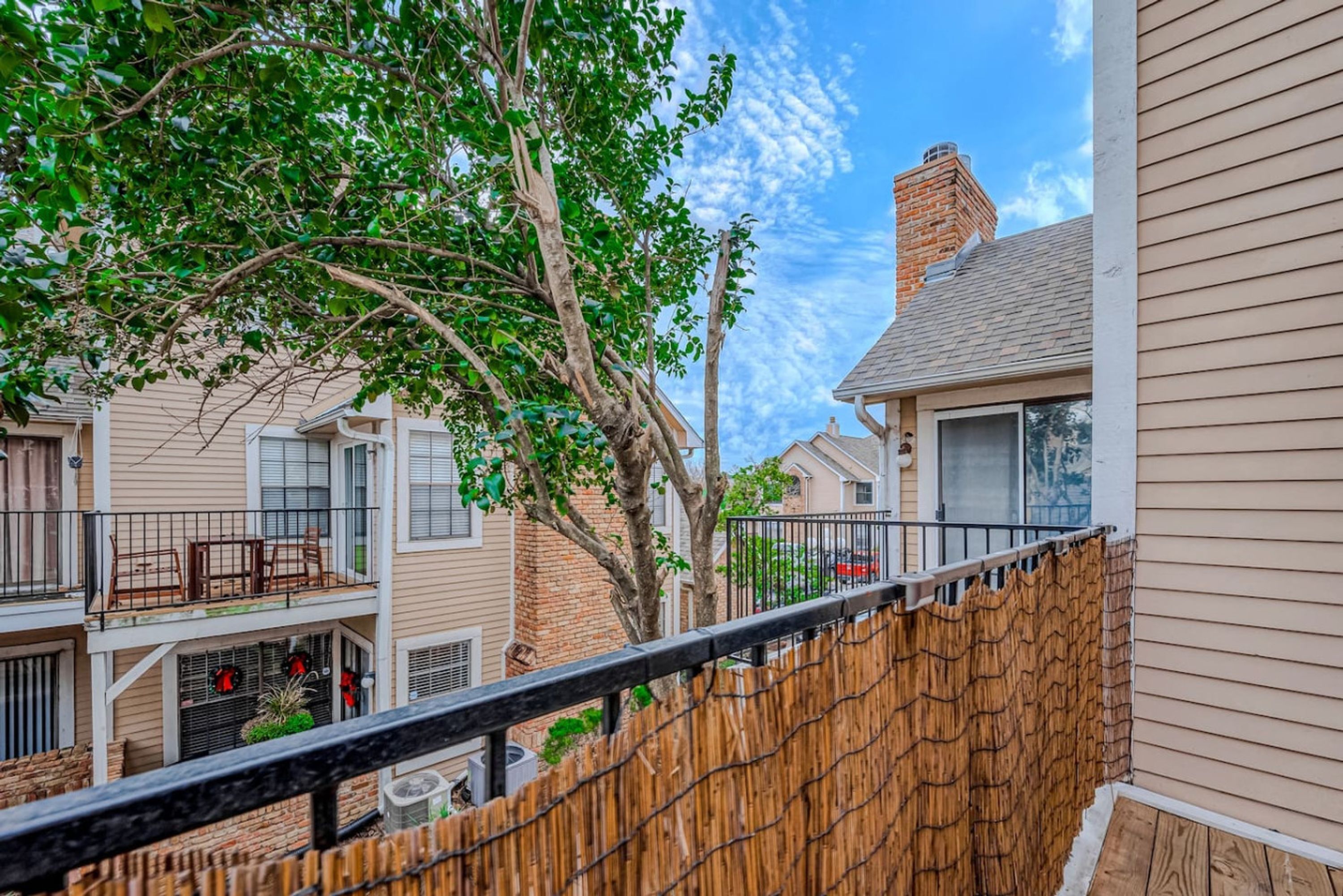 A residential building with a wooden deck, a brick chimney, and a fenced area with a wooden fence.