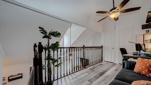 A spacious living area with a wooden staircase, a ceiling fan, and a view of the adjacent room. - Upscale 1BR Condo in Med Center (Houston)