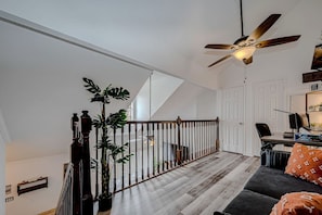 A spacious living area with a wooden staircase, a ceiling fan, and a view of the adjacent room.