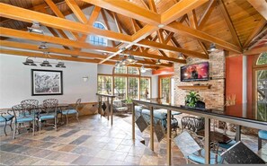 A spacious room with a high ceiling, wooden beams, a fireplace, and a large window. - Upscale 1BR Condo in Med Center (Houston)