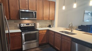 A modern kitchen with wooden cabinets, stainless steel appliances, a microwave, oven, and dishwasher. - Elite Downtown Poolside Oasis (Houston)