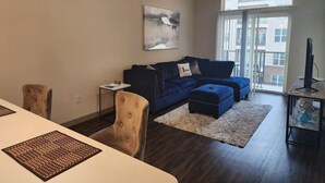 A living room with a dark blue sectional sofa, a white rug, a beige armchair, and a small side table. - Elite Downtown Poolside Oasis (Houston)
