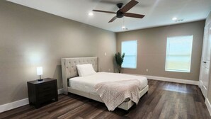 Une chambre à coucher comprenant un lit, une table de chevet, un ventilateur de plafond et deux fenêtres.