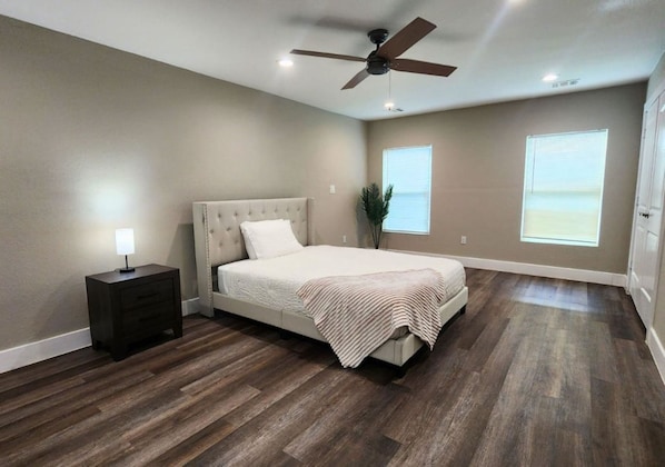 A bedroom with a bed, a nightstand, a ceiling fan, and two windows.