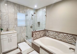 Ein modernes Badezimmer mit einer großen Badewanne, einer Duschkabine aus Glas und Marmorfliesen.