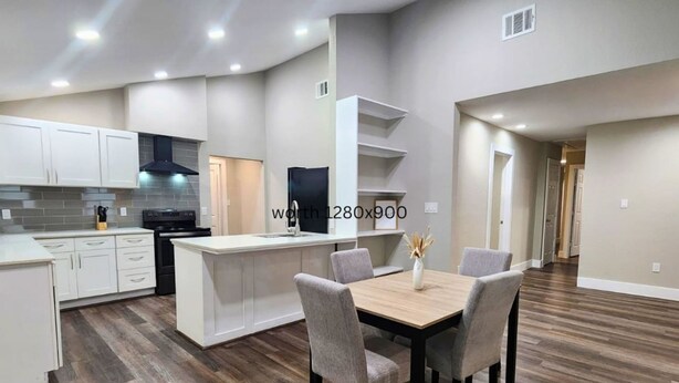 Une cuisine moderne avec des meubles blancs, une cuisinière noire et un coin repas comprenant une table en bois et quatre chaises.