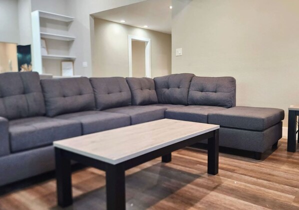 A modern living room with a sectional sofa, a coffee table, and wooden flooring.