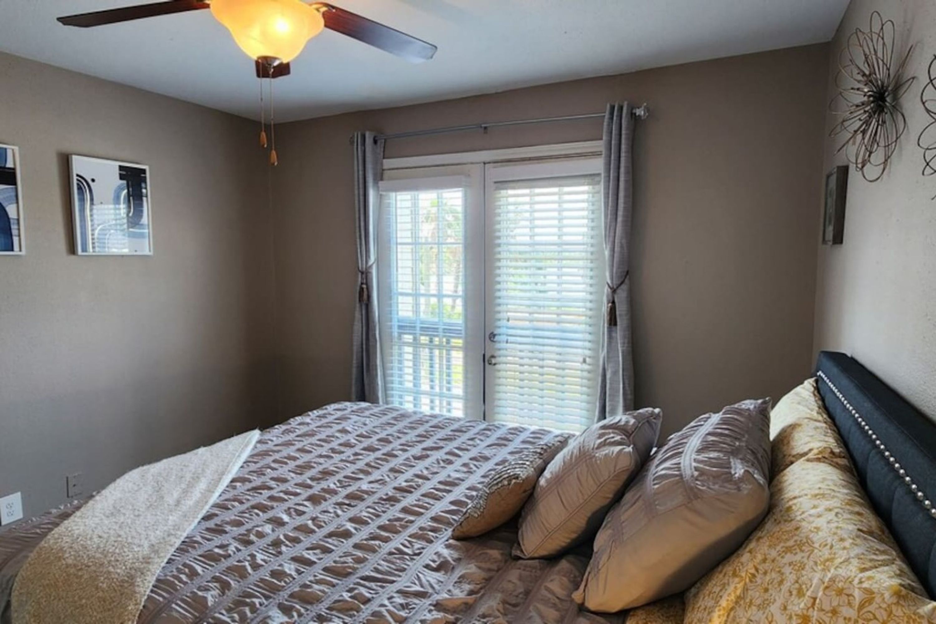 Un dormitorio con cama, ventilador de techo y ventana con persianas.
