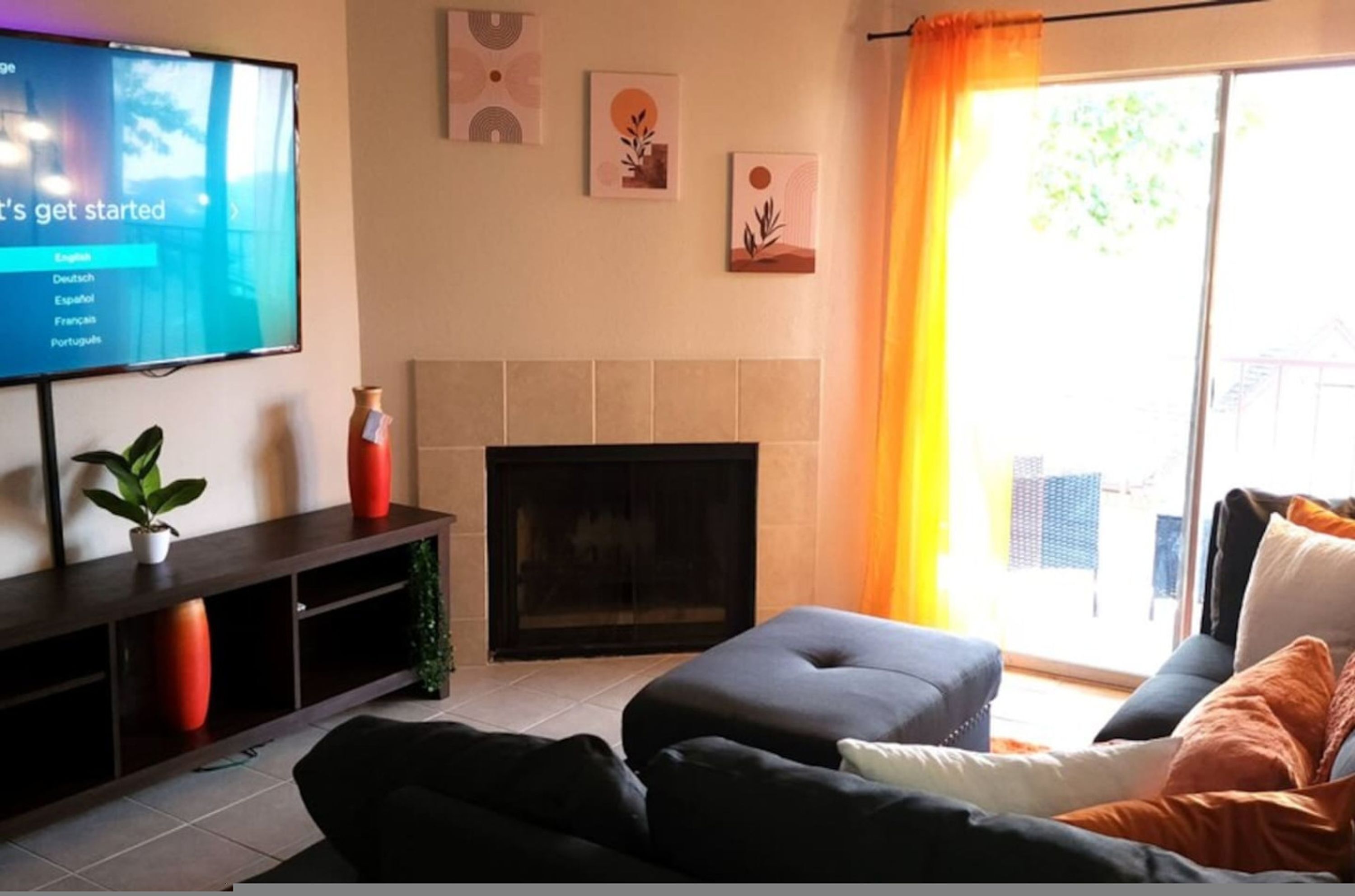 A living room with a flat-screen TV, a fireplace, a sofa, and a sliding glass door with curtains.