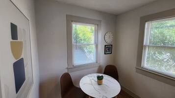 A small room with two windows, a clock, and a framed picture on the wall.