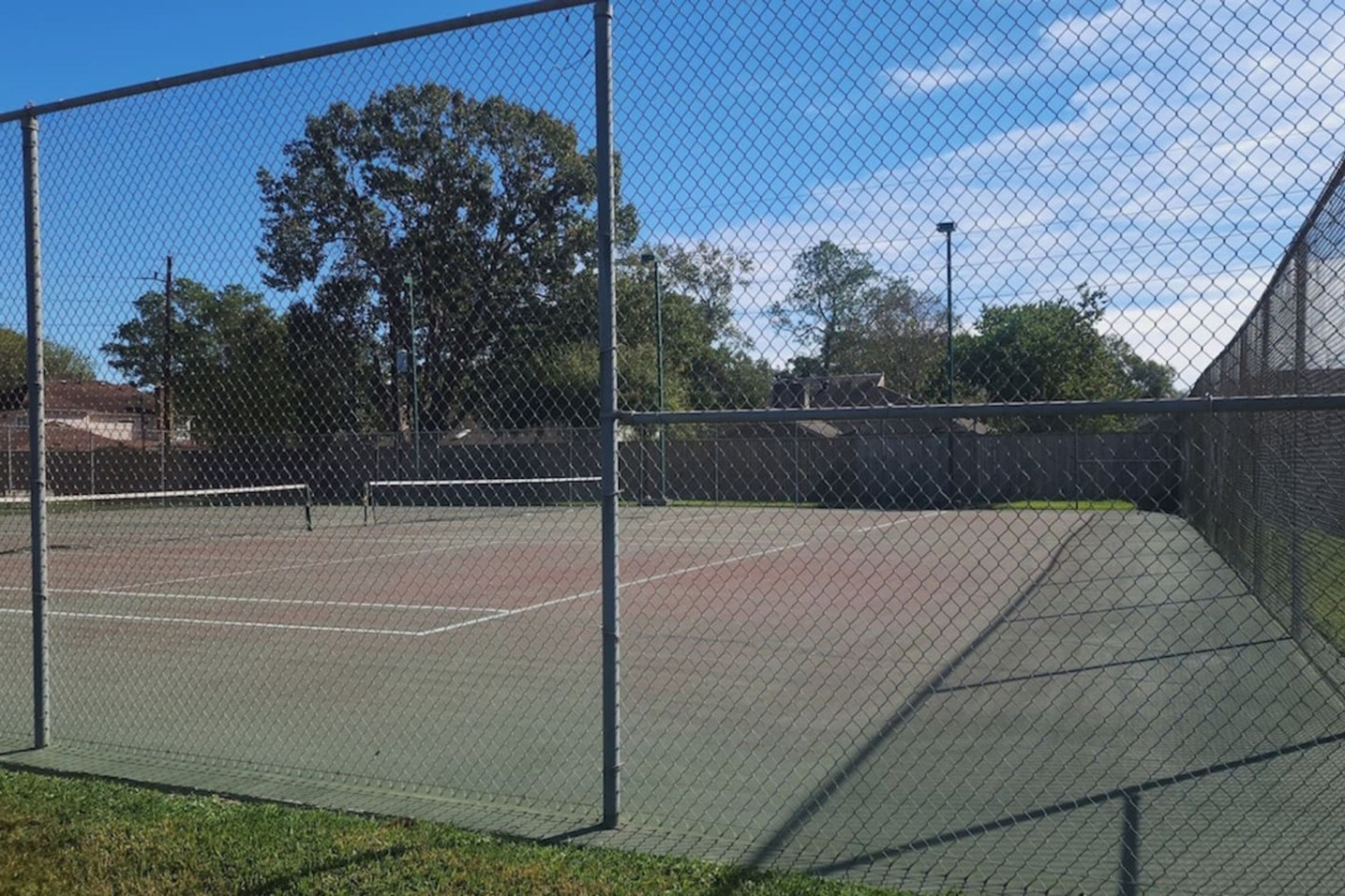 A tennis court enclosed by a chain-link fence with a net in the center.