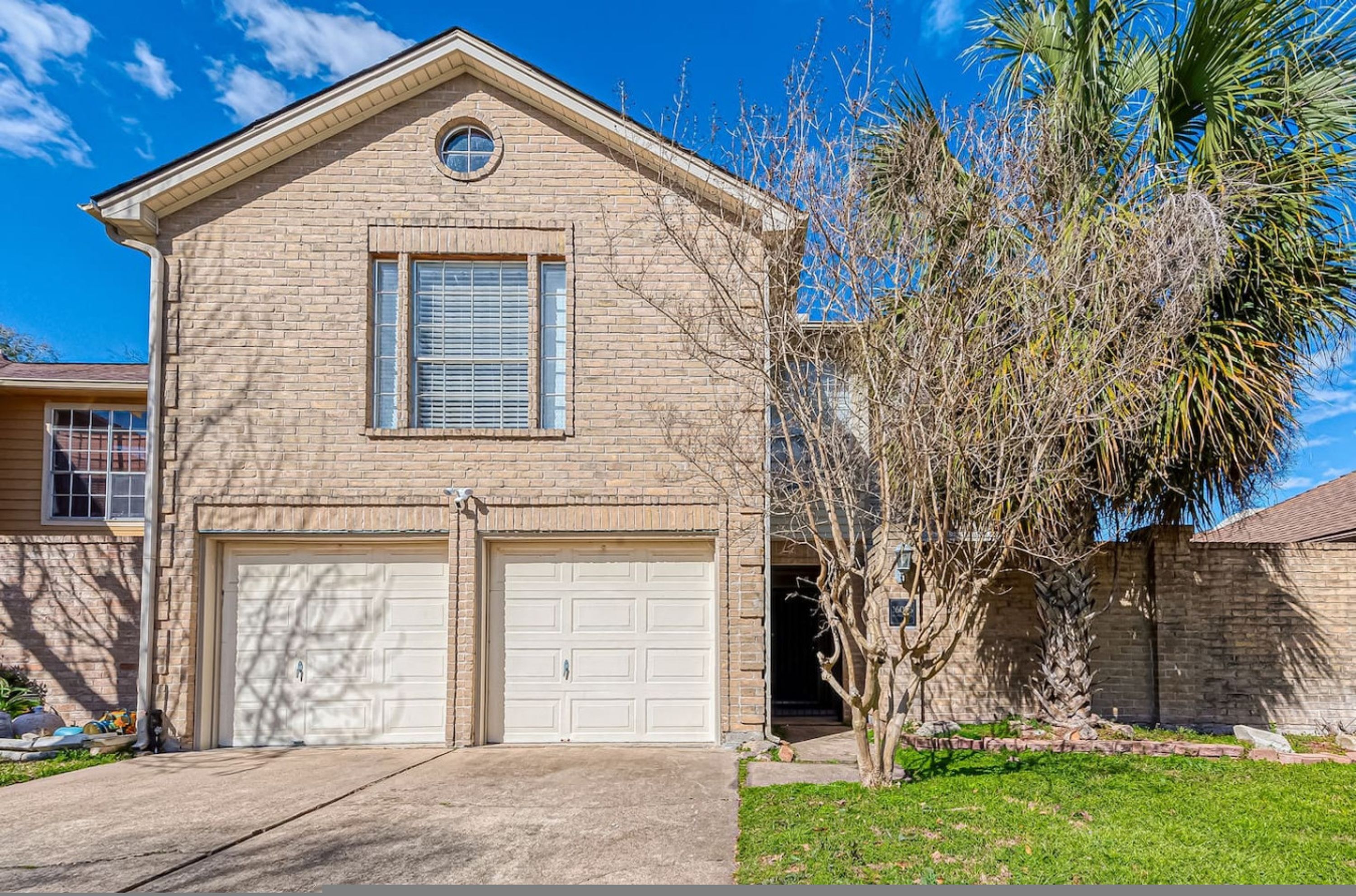 A two-story house with a garage, a small window, and a tree in the front yard.