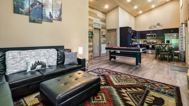 A living room with a sofa, ottoman, and a pool table. There is a kitchen area with cabinets and appliances. - Mountain Cabin Getaway Jacuzzi Stunning Views (Sevierville)