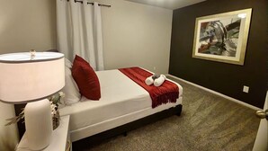 A neatly arranged bedroom with a bed, a bedside lamp, a wall-mounted painting, and a door. - Serenity in Suburbia - Katy Tx (Katy)