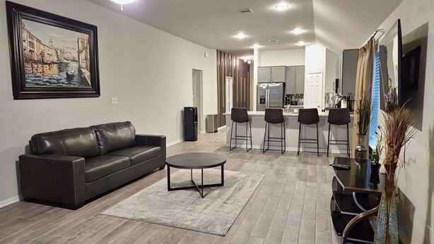 A modern living room with a dark leather sofa, a round coffee table, and a painting of a cityscape on the wall. - Serenity in Suburbia - Katy Tx (Katy)