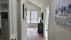 A hallway with a wooden floor, a door on the left, and a painting on the right. - City Living Near Med Center NRG and Downtown (Houston)