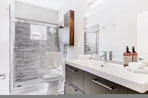 Un bagno moderno con cabina doccia in vetro, un water bianco, un mobile lavabo con specchio e articoli da toilette.