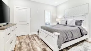 Ein Schlafzimmer mit Bett, Kommode, Fernseher und Deckenventilator.