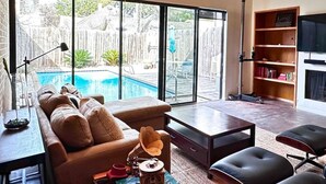 A spacious living room with a large window overlooking a swimming pool and a wooden deck. - Private Pool Oasis Montrose Retreat Sleeps 8 (Houston)