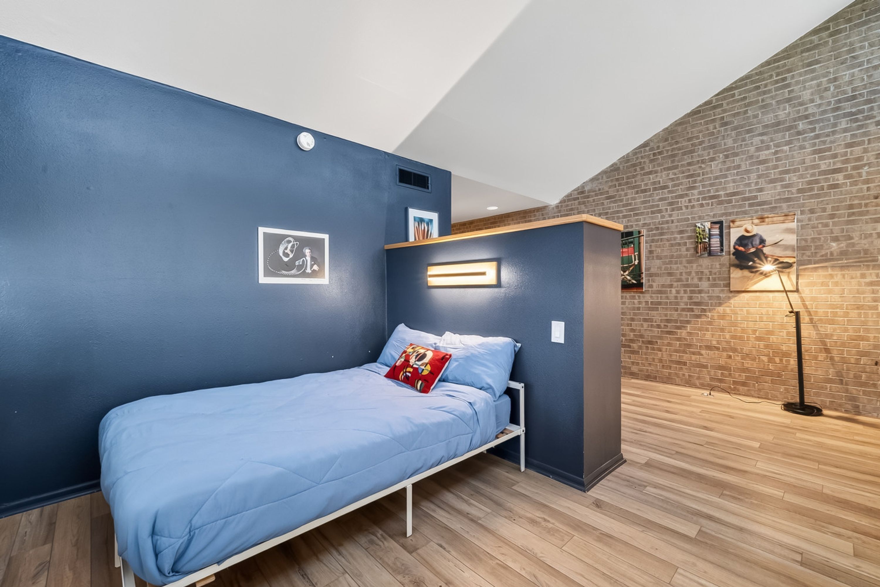 A compact room with a single bed, a small seating area, and a brick wall.