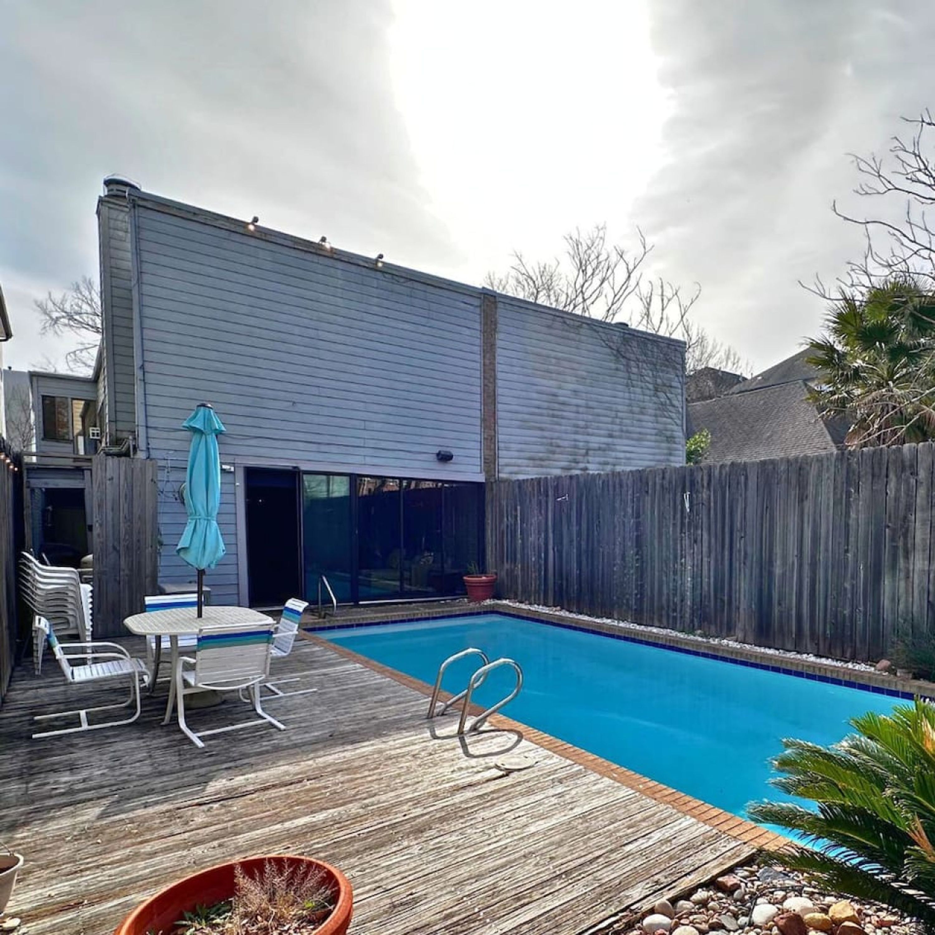 Un jardin avec une piscine, une terrasse en bois et un espace patio aménagé avec des chaises et une table.