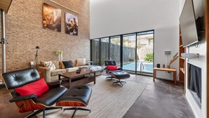 A spacious living area with a brick wall, modern furniture, and a large TV. - Private Pool Oasis Montrose Retreat Sleeps 8 (Houston)
