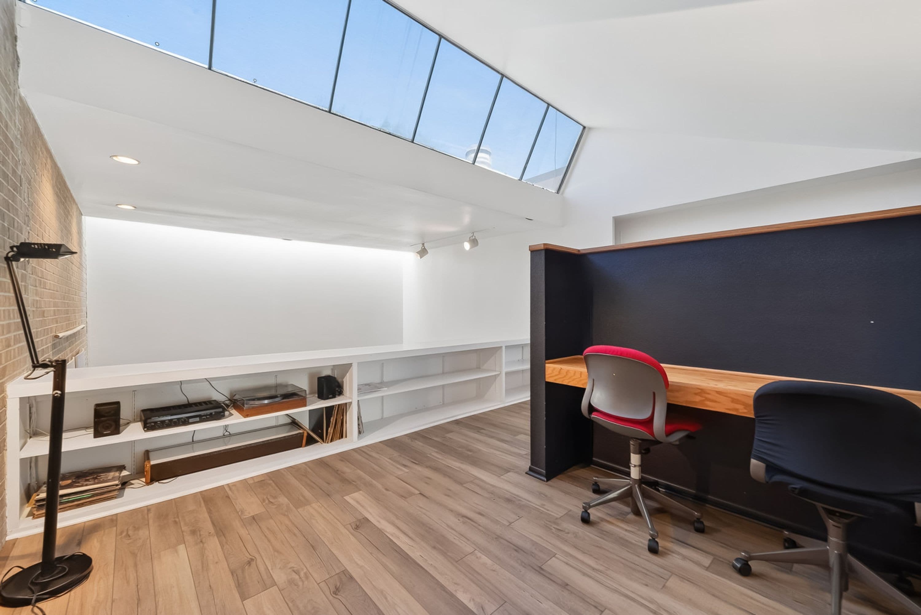 Un espacio de oficina moderno con tragaluz, suelo de madera, un escritorio, dos sillas y una estantería.